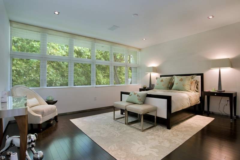 Bedroom with dark wood floors, shades of white with some brown, and a wall of windows